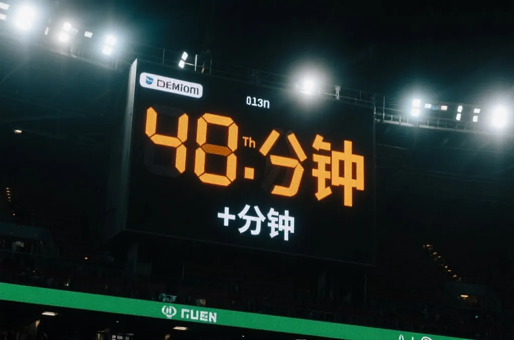 體育場大型電子計分板特寫,顯示第90分鐘及傷停補時的發光數字,充滿緊張感